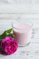 Ayurvedic drink pink milk or matcha. A glass of refreshing cocktail stands on a wooden white background. Nearby lies a lilac rose