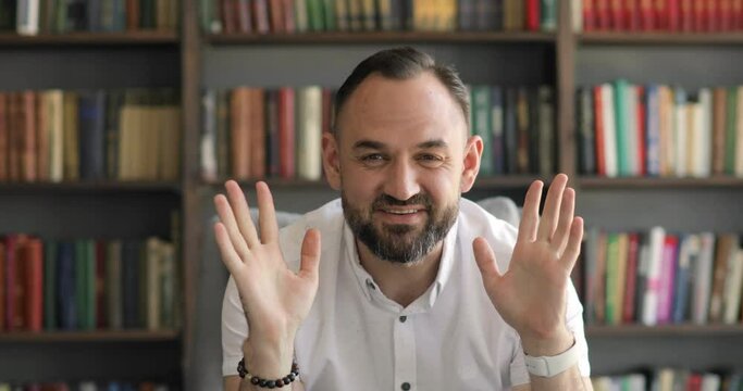 Mature man talking calling video call, listening and nodding head to answer in office, library on bookshelves background. First person view. Remote work of teacher, professor or entrepreneur online.