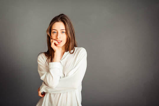 Young girl in a white shirt, hands up, on a gray background. Honest and emotional on the banner, billboard, billboard. No retouch. Without make-up.