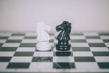 The white and black knight chess faces one another on the chessboard.