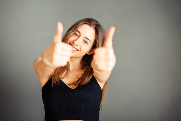 Fototapeta premium Girl in a black top with her hair shows thumb up. On a gray background. Without makeup, without retouching.