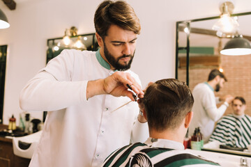 handsome barber cutting the hair of a young brunette in the barber shop 