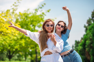 Two beautiful girls spring in the park on a sunny summer day. Sisters walk in fashionable outfits...