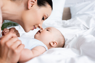 selective focus of beautiful mother looking at infant son lying on bed