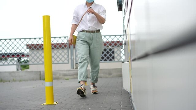 Masked girl takes her order in a box from a cell. Contactless delivery. Parcel lockers. Woman client using automated self service post terminal machine or locker to receive a parcel
