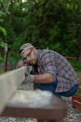 Handsome young man carpenter installing a wood fence outdoor terrace in new house. Wearing safety glases and gloves .