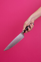 Female hand with kitchen knife isolated on pink background