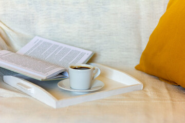 A small Cup of coffee and an open book against a warm blanket.The concept of relaxing in a cozy home environment.