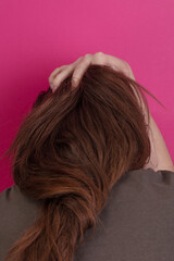 Fototapeta premium Woman with the shaggy long hair turns her face into the pink wall, feeling tired and sad.