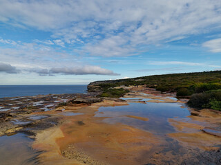 Fototapeta na wymiar Beautiful coastal trail with colorful rock formations and reflections of blue sky on water puddles near Wattamolla Beach, Royal National Park, New South Wales, Australia