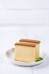 Castella (kasutera) - Beautiful delicious Japanese sliced sponge cake food on white plate over rustic white wooden table, close up, copy space design concept.