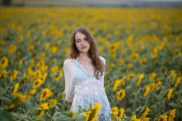 Beautiful young girl posing in a sunflower field at sunset 