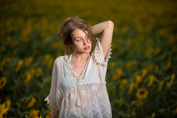 Beautiful young girl posing in a sunflower field at sunset 