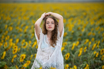 Beautiful young girl posing in a sunflower field at sunset 