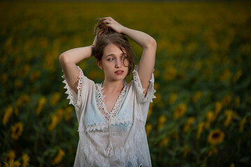 Beautiful young girl posing in a sunflower field at sunset 
