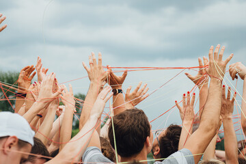 Hands of people, connected by a thread, during a open air corporate team building. Team building...