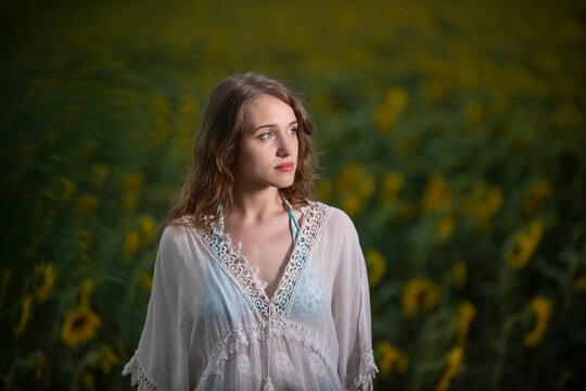 Beautiful young girl posing in a sunflower field at sunset 