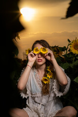 Beautiful young girl posing in a sunflower field at sunset 