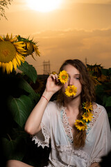 Beautiful young girl posing in a sunflower field at sunset 
