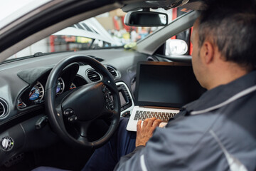 Analysis of a car in the workshop. The mechanic's inside the car checking the data from the laptop.