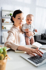 selective focus of mother typing on laptop keyboard and holding in arms baby boy