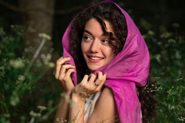 Happy young girl posing with a purple scarf on forest background