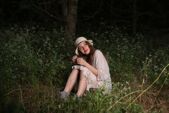 Beautiful young girl with a straw hat posing in a dark forest