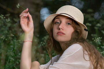 Beautiful young girl with a straw hat posing in a dark forest