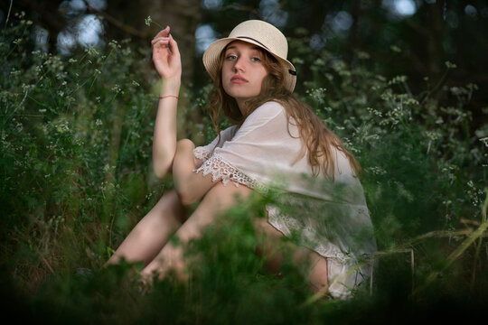 Beautiful young girl with a straw hat posing in a dark forest