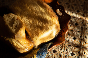 a Golden loaf of bread and a slice of sliced loaf lie in a basket on the kitchen table on a tablecloth with a floral pattern of the house a play of light and shadow