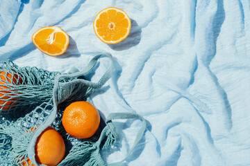 Picnic flatlay of oranges in an eco string bag on blue blanket