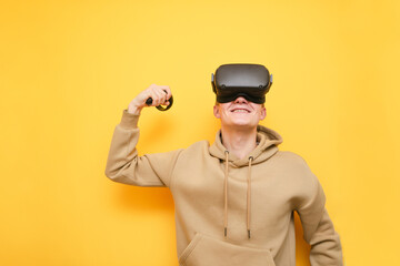 Happy VR gamer winner stands on yellow background, smiles and shows biceps. Portrait of a guy in a VR helmet smiling isolated on yellow. Virtual Reality Cocnept. Copy space