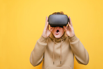 Closeup portrait of shocked guy in virtual reality helmet on yellow background, with shocked face looking into VR glasses screen. Young man surprised by reality VR helmet. Isolated.