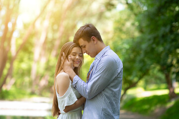 Fototapeta premium Affectionate young man caressing his girlfriend's face and hugging her outdoors