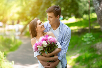 Young husband and wife with flower bouquet celebrating birthday outside on summer day