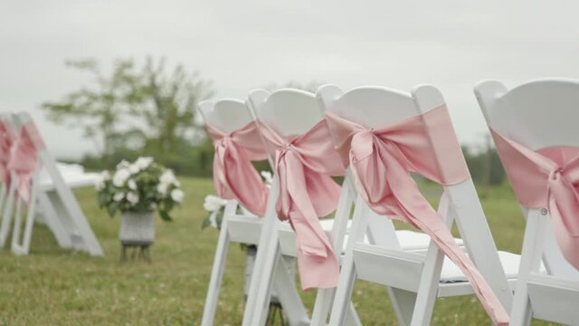 White Chairs In First Row of Wedding Reception With Pink Bows