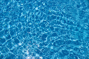 Abstract background with clear water in the swimming pool, bright blue water with sun reflection. Concept of summer/ sea vacation. Ripple water and gentle wave