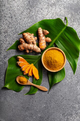 Turmeric powder and fresh turmeric root on grey concrete background.