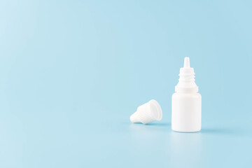 Eye drop or ear drop bottle on light blue background. Blank white plastic container for fluid. Pharmaceutical packaging product.