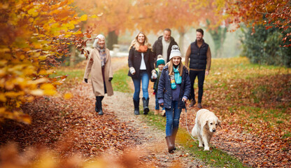 Fototapeta premium Multi-Generation Family Walking With Pet Golden Retriever Dog Along Autumn Woodland Path