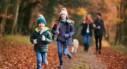 Family Walking With Pet Golden Retriever Dog Along Autumn Woodland Path Together