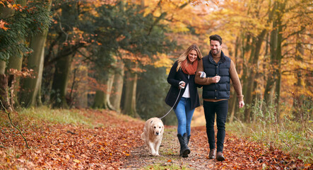 Loving Couple Walking With Pet Golden Retriever Dog Along Autumn Woodland Path Through Trees - Powered by Adobe