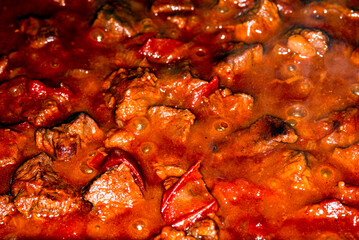 Traditional Hungarian goulash. Boiling beef stew with tomatoes and paprika, macro picture.