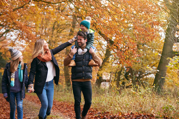 Family Walking Along Autumn Woodland Path With Father Carrying Son On Shoulders