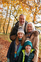Fototapeta na wymiar Portrait Of Grandparents With Grandchildren Enjoying Walk Along Autumn Woodland Path Together