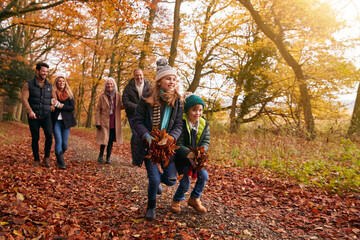 Children With Handful Of Leaves As Multi-Generation Family Walking Along Autumn Woodland Path