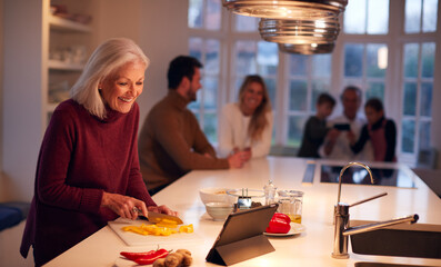 Senior Woman Preparing Meal For Family From Recipe On Digital Tablet