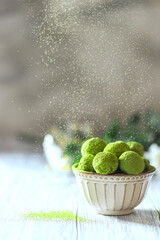 Homemade truffle sweets with green matcha tea in a ceramic bowl on a light wooden background. Raw energy balls.