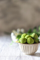 Homemade truffle sweets with green matcha tea in a ceramic bowl on a light wooden background. Raw energy balls.