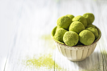 Homemade truffle sweets with green matcha tea in a ceramic bowl on a light wooden background. Raw energy balls.
